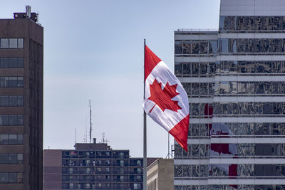 Low angle view of flag against buildings in city against clear sky