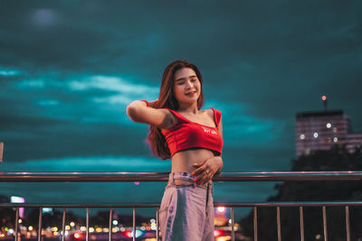Woman standing against railing in city at night
