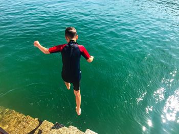 Full length rear view of boy jumping in the sea 