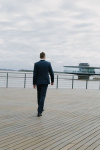 Rear view of man standing on pier over sea against sky