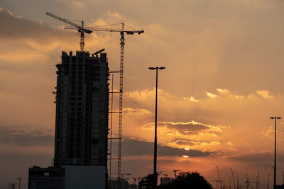 Low angle view of crane by building against sky during sunset