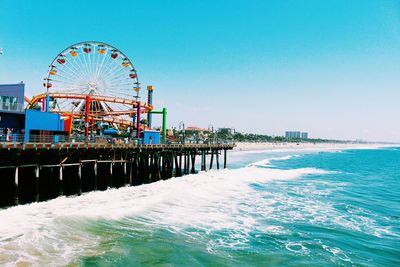 Ferris wheel by sea against clear blue sky