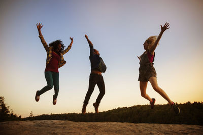 Friends jumping on rock against clear sky during dusk