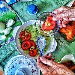 Cropped hands holding bowl and spoon over food on table