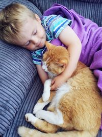 High angle view of boy lying with ginger cat on sofa at home