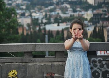 Portrait of cute girl gesturing peace sign while standing against retaining wall