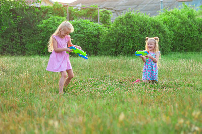 Two little girls play in the summer on a green meadow with water pistols