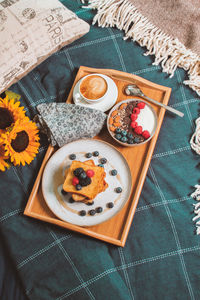 Breakfast in bed from above, yogurt bowl with berries, french toasts, coffee cup on wooden plate