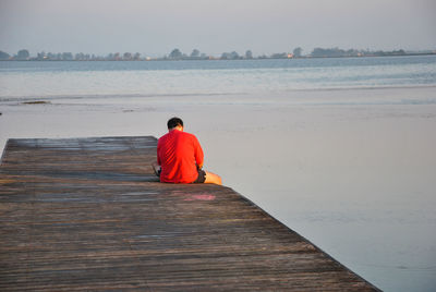 Rear view of man sitting on pier over sea against sky