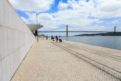 People on bridge over sea against cloudy sky