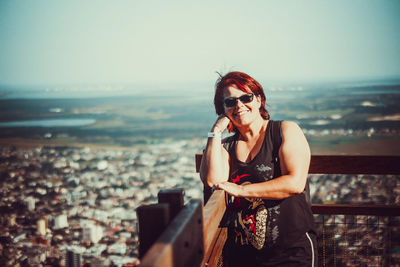 Young woman wearing sunglasses standing by cityscape against sky