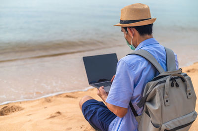 Rear view of woman using mobile phone while sitting at beach