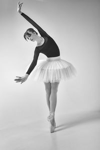 A ballerina in a bodysuit and tutu poses in motion showing ballet elements while standing on pointes