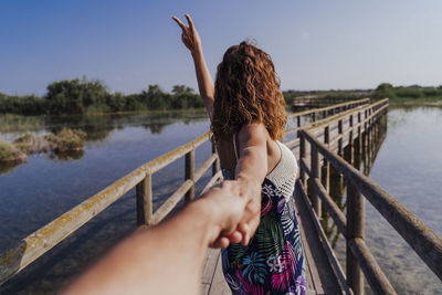 Young woman with arms raised in lake against sky