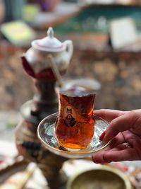 Cropped hand holding tea in glass on saucer