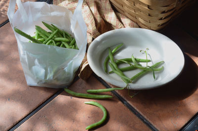 Green beans, white dish with prepared green beans ready for cooking, basket on outdoor table