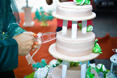 Midsection of couple cutting wedding cake