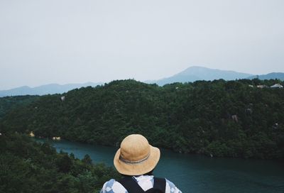 Rear view of person hat by river against sky