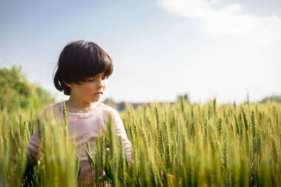 Side view of girl with dark short hair in pink top standing in green wheat field