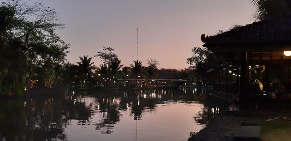 Silhouette trees by lake against sky at sunset