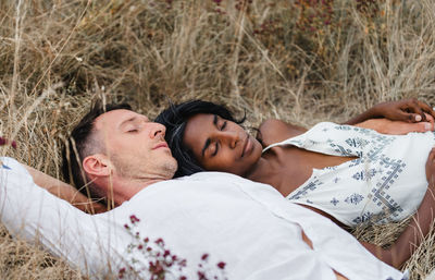 Unshaven man with indian female partner sleeping on meadow in daytime