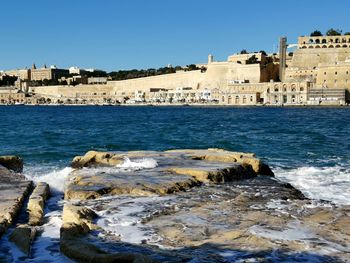 Buildings by sea against clear blue sky