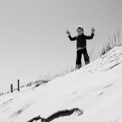 Boy standing with arms raised on snowcapped mountain against clear sky