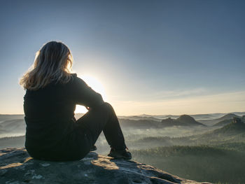 Peaceful landscape. pretty girl sitting on the rocks, looking far away. sportswear on her slim body
