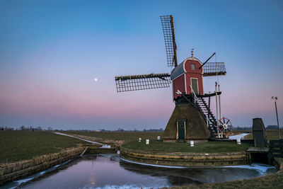 Traditional windmill on field against sky at sunset