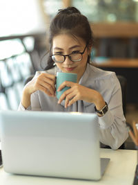 Businesswoman holding coffee cup while sitting in office