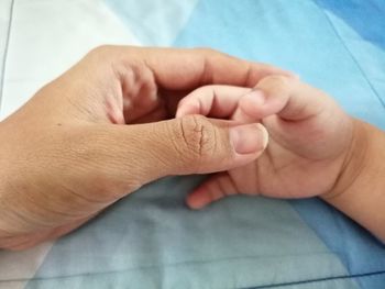 Cropped image of parent holding baby hands on bed