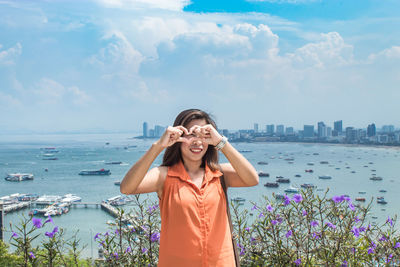 Woman making heart shape with hands against sea 