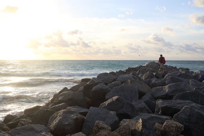 Man sitting on rock at sea shore against sky