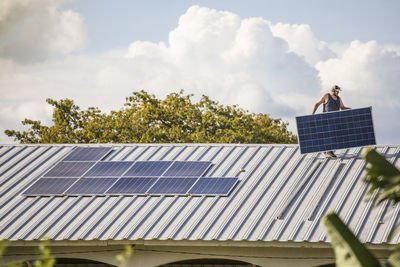 Man carrying solar panel on rooftop.