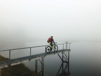 Man riding bicycle on riverbank against sky