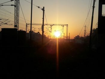 Silhouette electricity pylons against sky during sunset