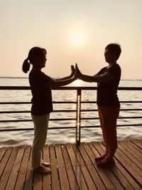 Full length of friends standing on pier over sea against sky during sunset