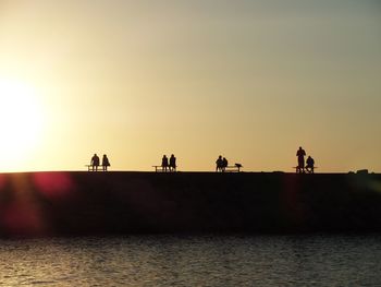 Silhouette people by sea against clear sky during sunset