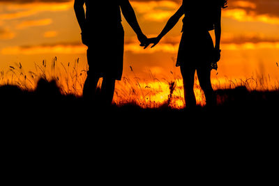 Silhouette men standing on field against orange sky