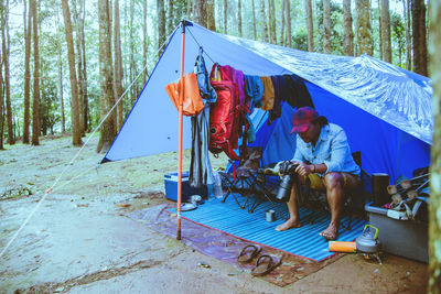 Man holding camera while sitting in tent at forest