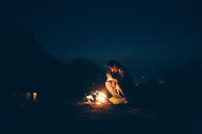 Man crouching by campfire at night