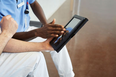 High angle view of male nurses discussing over digital tablet while sitting in corridor at hospital