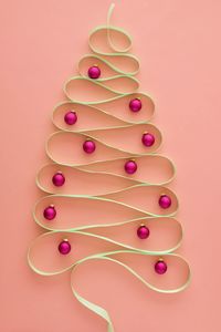 Directly above view of ribbon christmas tree and decorations against pink background. 