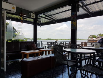 Empty chairs and tables in restaurant by sea against sky