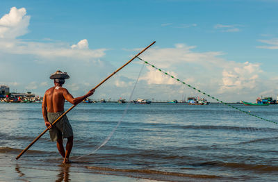 Rear view of fisherman fishing in sea against sky