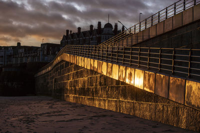 Bridge over river against buildings at sunset