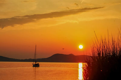 Silhouette sailboats in sea against orange sky