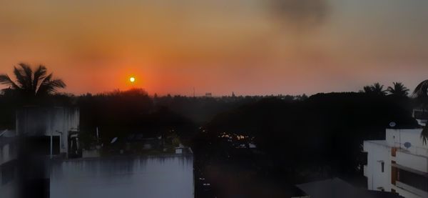 Silhouette trees and buildings against sky during sunset