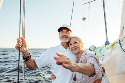 Smiling senior couple on sailboat in sea against sky