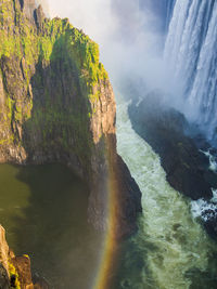 Scenic view of detail of victoria falls with overgrown cliff and rainbow